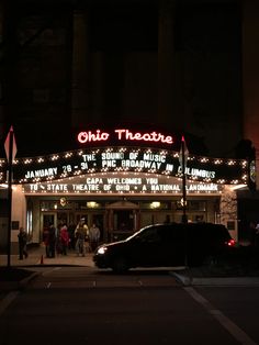 the theatre is lit up at night with people walking around