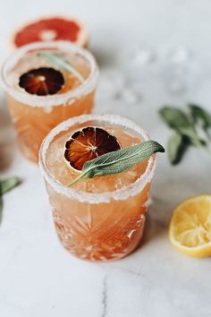 two glasses filled with orange juice and garnished with sage leaves, sitting on a marble surface