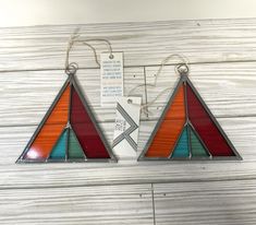 two colorful stained glass hangings on a white wooden wall with tags attached to them