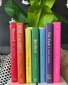 four books are stacked on top of each other in front of a potted plant