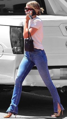 a woman walking down the street talking on her cell phone while wearing jeans and heels