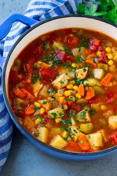 a blue pot filled with vegetable soup and garnished with parsley on the side