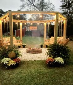 an outdoor fire pit surrounded by plants and hanging lights in the middle of a yard