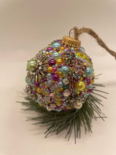 a christmas ornament is hanging on a pine branch with beads and other decorations