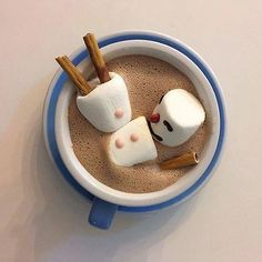 two marshmallows in a cup with cinnamon sticks sticking out of them to look like faces