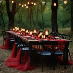 a long table with red cloths and candles on it in the middle of a forest