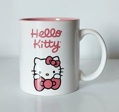 a hello kitty coffee mug sitting on top of a white table next to a wall