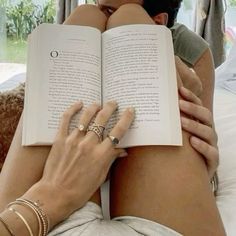 a woman laying on top of a bed holding an open book in her lap and reading it