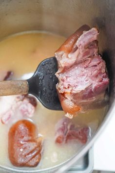 a pot filled with meat and sauce on top of a stove next to a wooden spoon