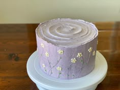 a purple cake with white flowers on it sitting on top of a wooden table next to a plate