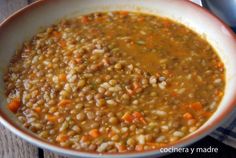 a bowl filled with lentils and carrots on top of a table next to a spoon