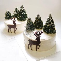 two cakes decorated with christmas trees and reindeer silhouettes on white frosted icing