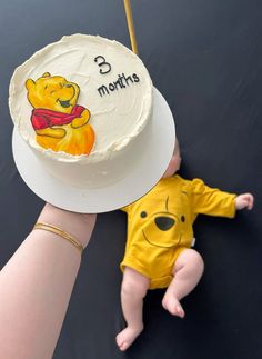 a baby laying on the ground next to a winnie the pooh cake and a hand holding it