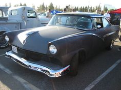 an old black car parked in a parking lot next to other antique cars and people