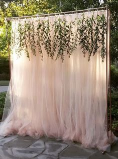 an outdoor wedding ceremony with pink tulle and greenery hanging from the ceiling,