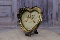 an ornate heart shaped clock with a crown on it's face sitting on a table