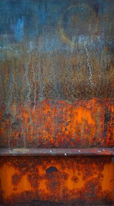 an old rusted metal bench sitting in front of a wall