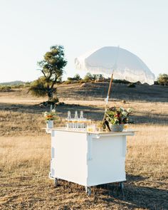 an outdoor bar set up in the middle of a field with an umbrella over it