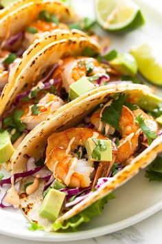 shrimp and avocado tacos on a white plate with limes, cilantro, red onion, and lettuce