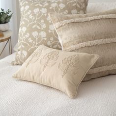 pillows on a bed with white linens and flowers in the middle, along with a potted plant