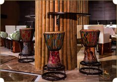 three large drum stands in front of a bamboo wall with chairs and tables behind them