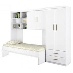 a white bedroom with a bed, bookcase and cupboards on the wall next to it