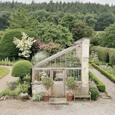 a small greenhouse in the middle of a gravel area with potted plants on either side