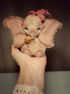 a hand holding a small stuffed animal in it's right hand and wearing a pink bow