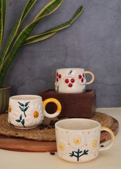 three coffee cups sitting on top of a wooden tray next to a potted plant