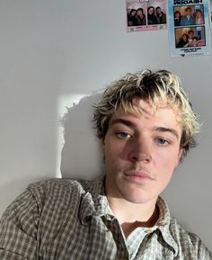 a young man with blonde hair is leaning against a white wall and looking at the camera