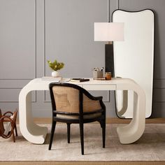 a white desk with a mirror and chair next to it on a rug in front of a gray wall