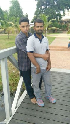 two young men standing on a wooden deck next to each other and posing for the camera