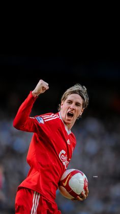 a man in red uniform holding a soccer ball with his mouth wide open and fist raised