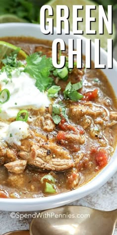 a white bowl filled with green chili and topped with sour cream, cilantro