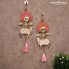 two pink and gold earrings hanging on a wall next to a vase with flowers in it