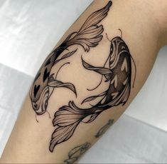 a black and white tattoo of two goldfish on the right arm, with one fish in its mouth