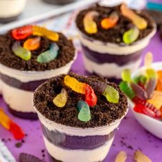 three desserts with gummy bears in them on a purple tray next to other treats