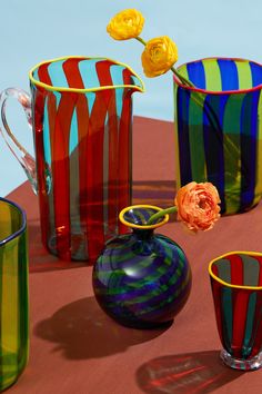 colorful glass vases and cups on a table with one flower in the foreground