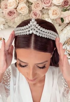 a woman wearing a tiara and holding her head up to her face with flowers in the background