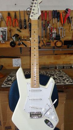 a white electric guitar sitting on top of a blue chair in a room filled with tools