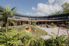 an empty playground in front of a large building with lots of trees and plants around it