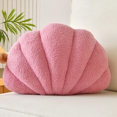 a pink pillow sitting on top of a white couch next to a potted plant