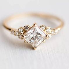 a gold ring with a princess cut diamond surrounded by small white and clear stones on the band