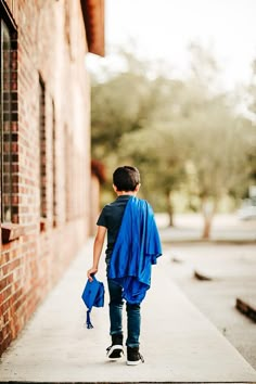 a young man walking down a sidewalk with a blue blanket on his back and an umbrella over his shoulder