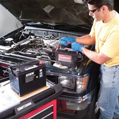 a man in yellow shirt working on an engine with two batteries and other tools next to his truck