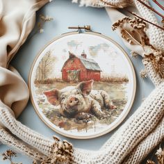 a cross stitch pattern with a pig laying on the ground in front of a barn