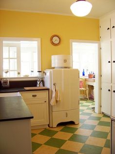 a kitchen with yellow walls and checkered flooring on the floor, white refrigerator freezer next to window