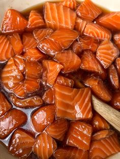 a bowl filled with sliced up salmon next to a wooden spoon