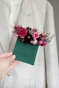 a person in a white suit holding a green piece of paper with flowers on it