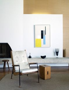 a chair and ottoman in a room with white walls, wood floors and artwork on the wall